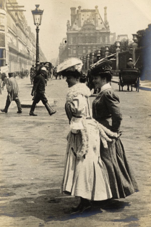 Two fashionable women cross the same boulevard, skirts lifted to avoid the dusty surface of the street, seemingly unaware of Sambourne’s camera.